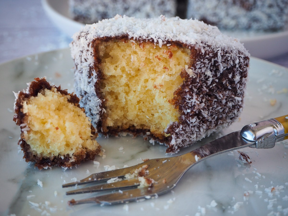 Lamingtons 38 Close up of lamington with a piece taken out with a fork and vintage cake for next to it.