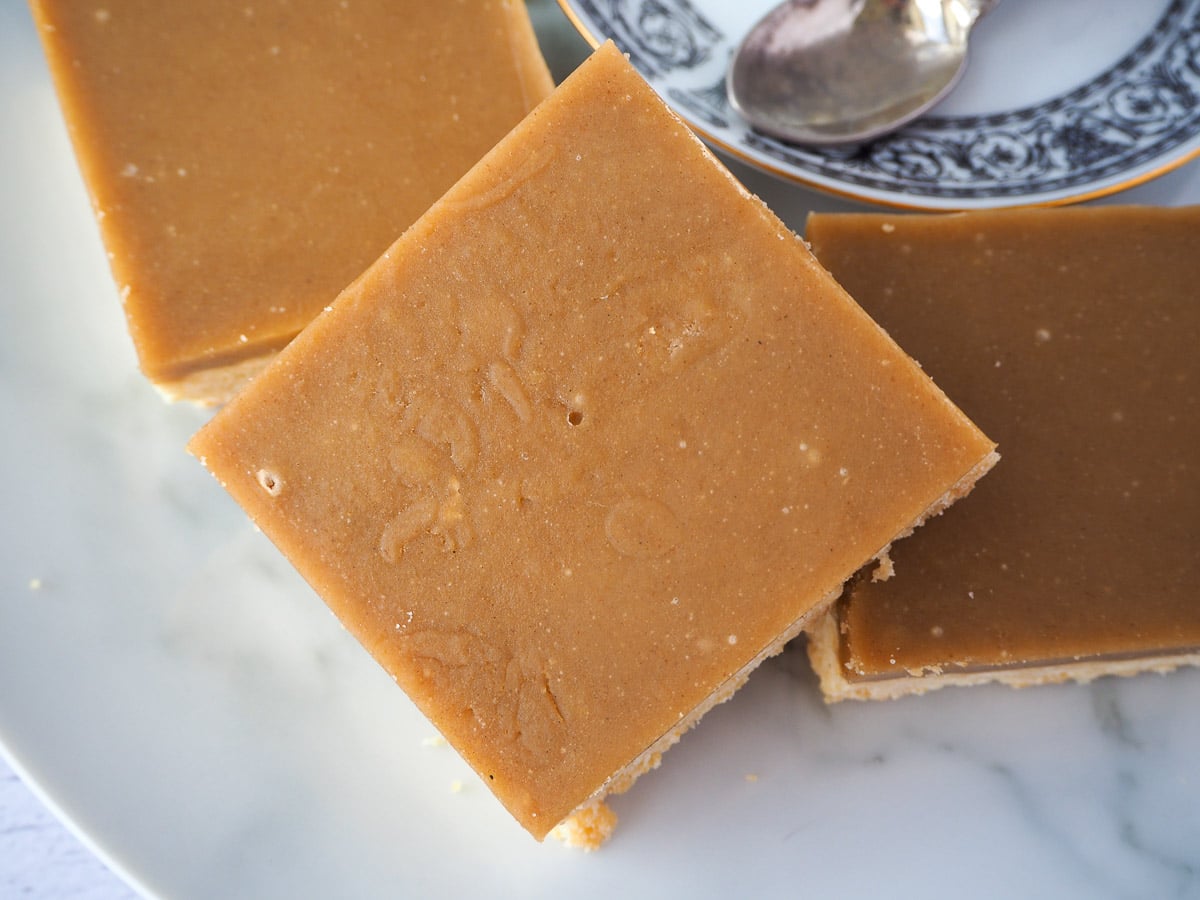 Ginger crunch 1 Close up of piece of ginger crunch stacked on top of other pieces, with a coffee saucer to the side.