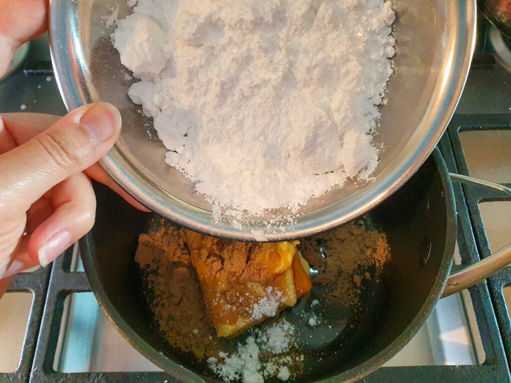 Ginger crunch 16 Adding sifted icing sugar to icing in pot on stove.