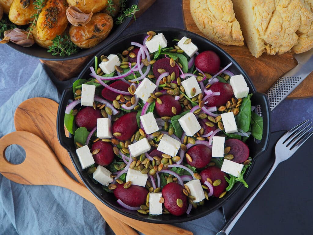 Beetroot salad 14 Beetroot salad on a plate, with damper and mini potatoes on the side, salad servers and a plate and fork.