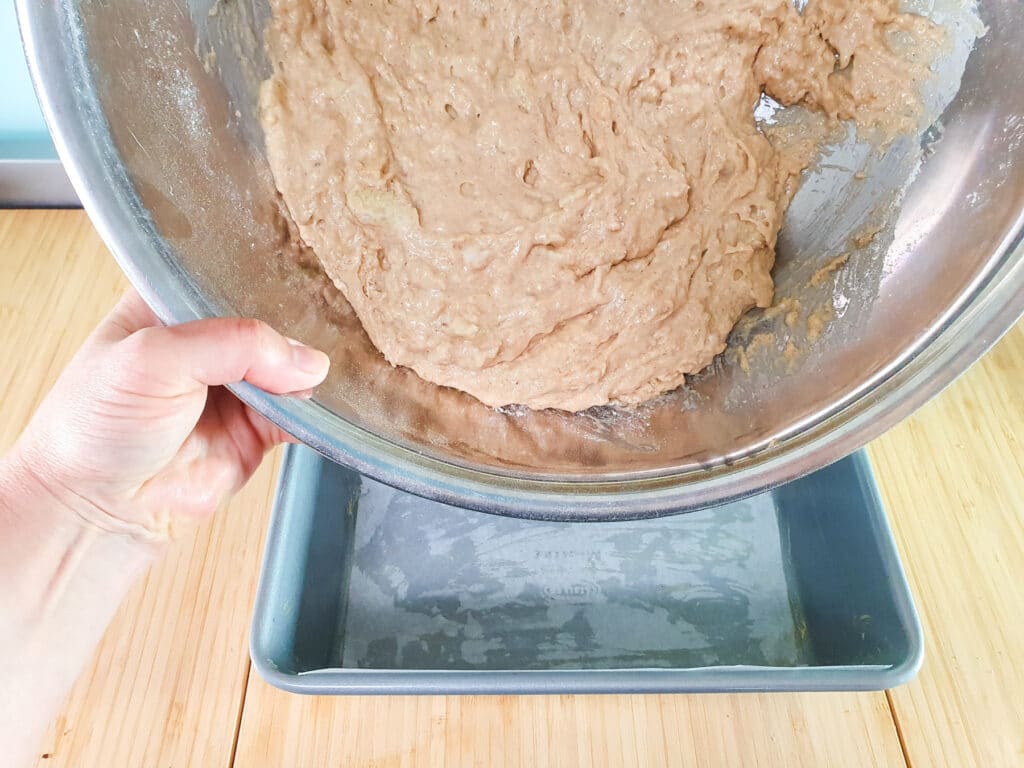 Tipping cake batter into loaf tin.
