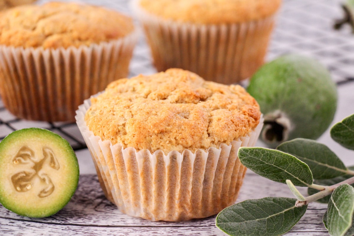 Feijoa muffins 16 Feijoa muffins with fresh feijoas and feijoa leaves, with extra muffins on a cooling rack in the background.