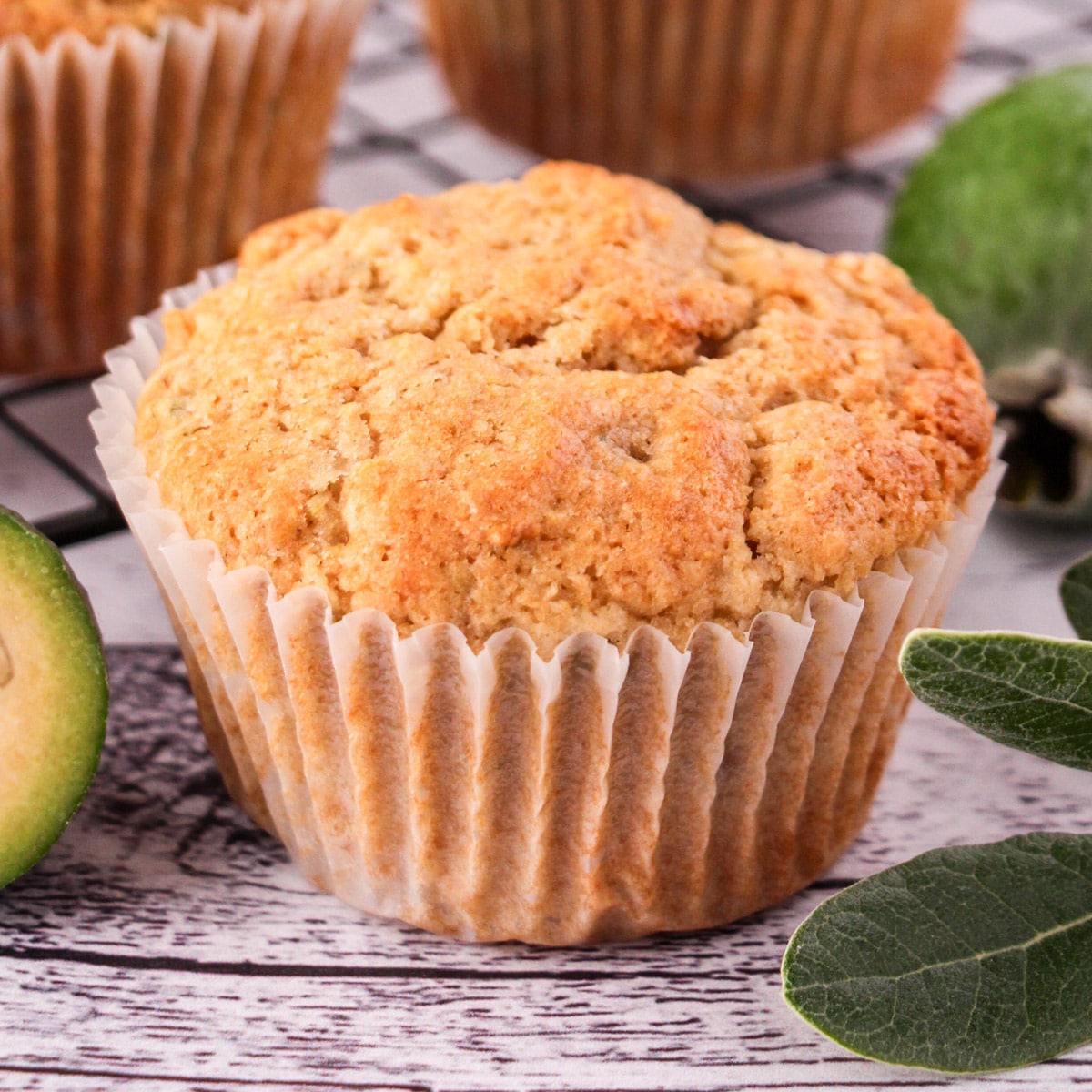 Feijoa recipes 11 Close up feijoa muffins with fresh feijoas and feijoa leaves, with extra muffins on a cooling rack in the background.
