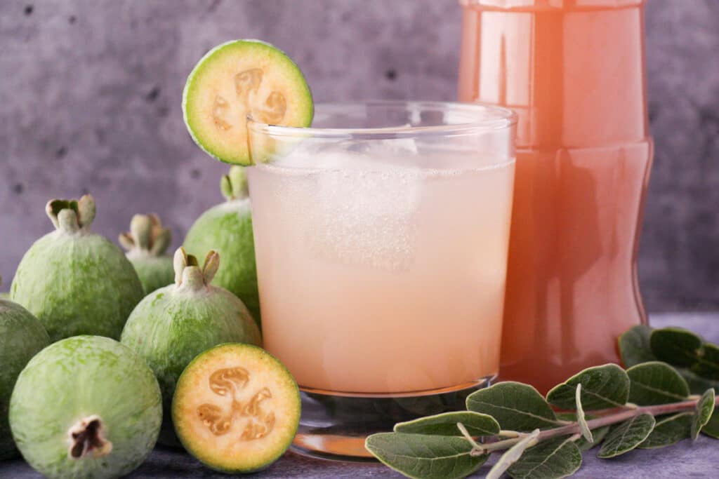 Feijoa recipes 24 Glass of made up feijoa syrup with ice and fresh feijoa garnish, with bottle of feijoa syrup and fresh feijoas and leaves.