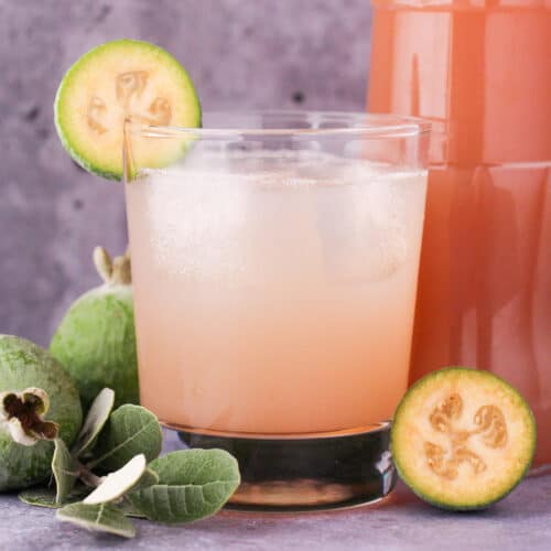 Feijoa syrup 21 Close up glass of made up feijoa syrup with ice and fresh feijoa garnish, with bottle of feijoa syrup and fresh feijoas and leaves.