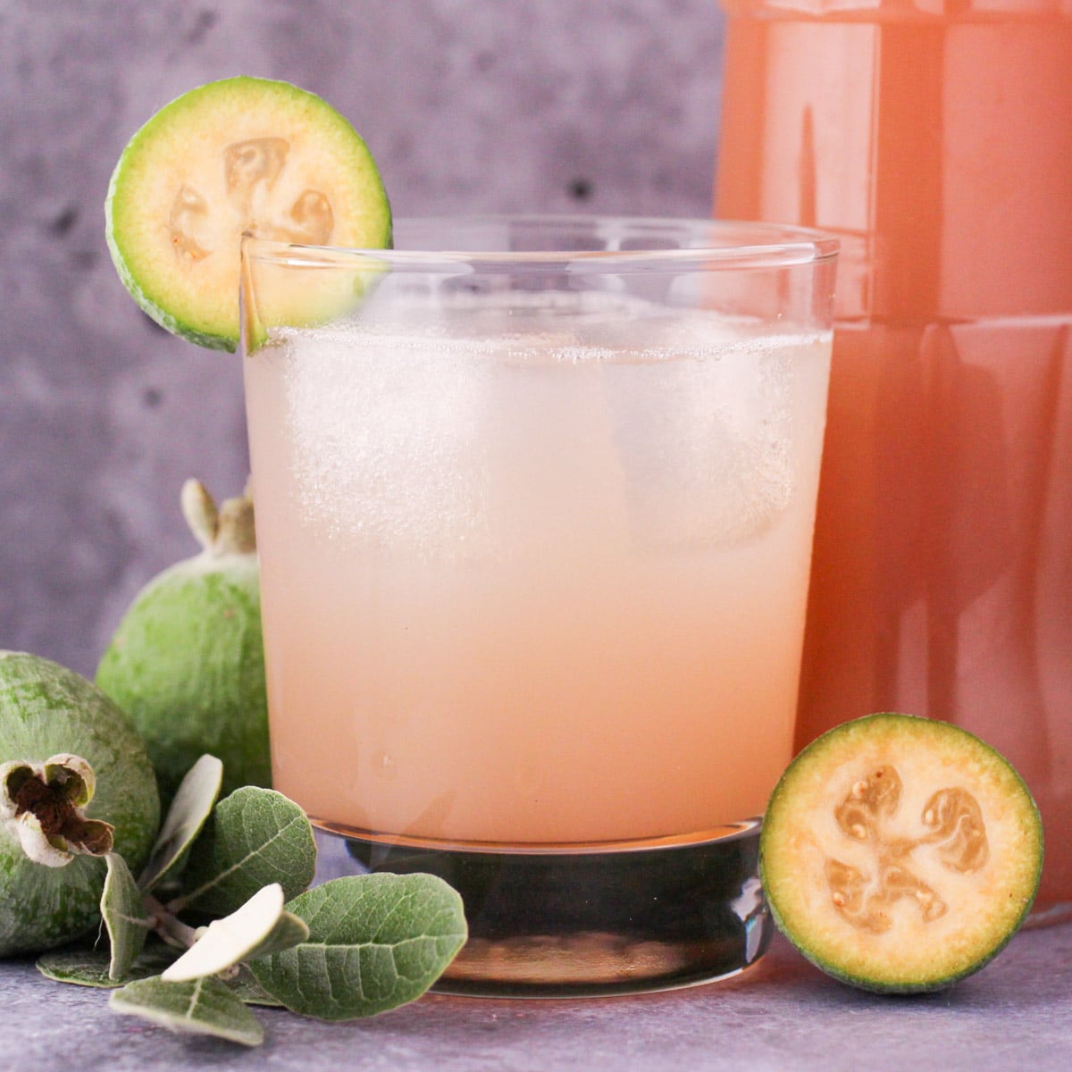 Feijoa recipes 25 Close up glass of made up feijoa syrup with ice and fresh feijoa garnish, with bottle of feijoa syrup and fresh feijoas and leaves.