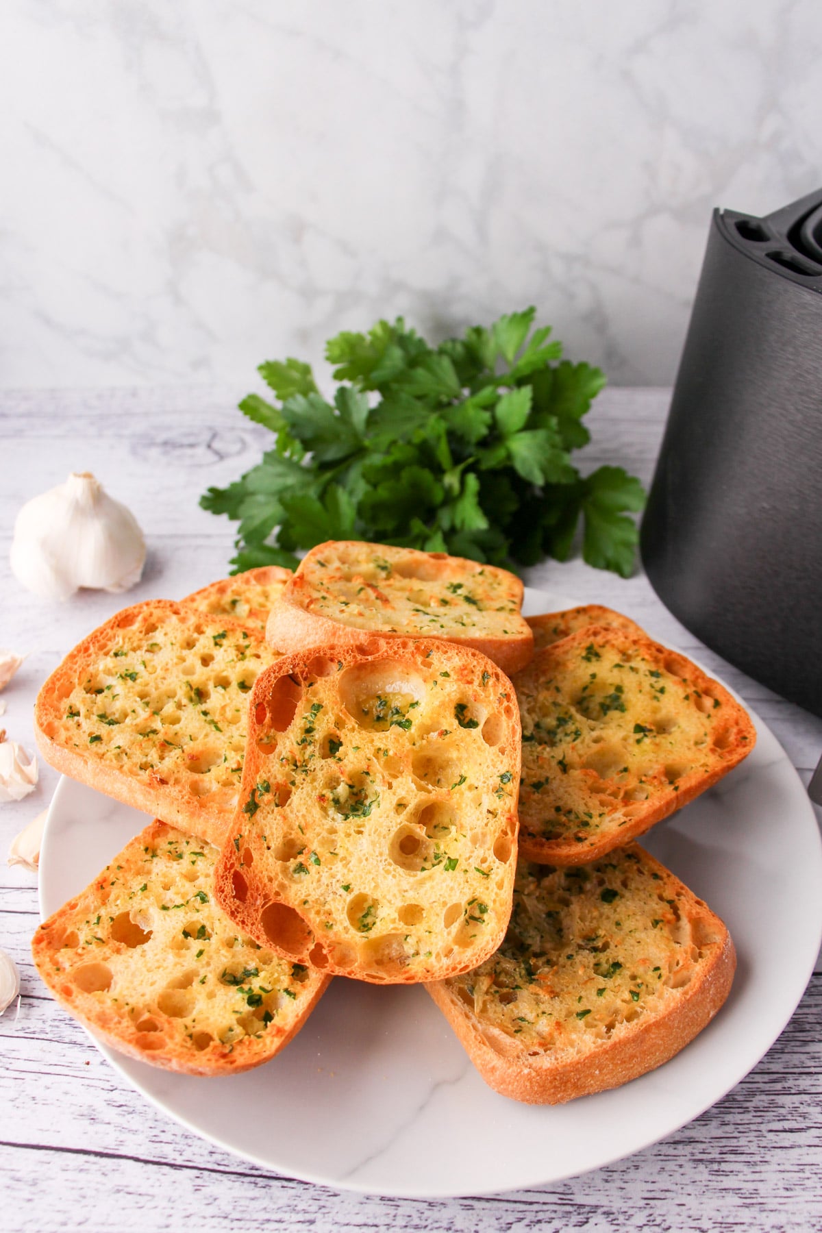 Air Fryer Garlic Bread 14 Stack of air fryer garlic bread on a plate, with air fryer basket and fresh garlic cloves to the sides.