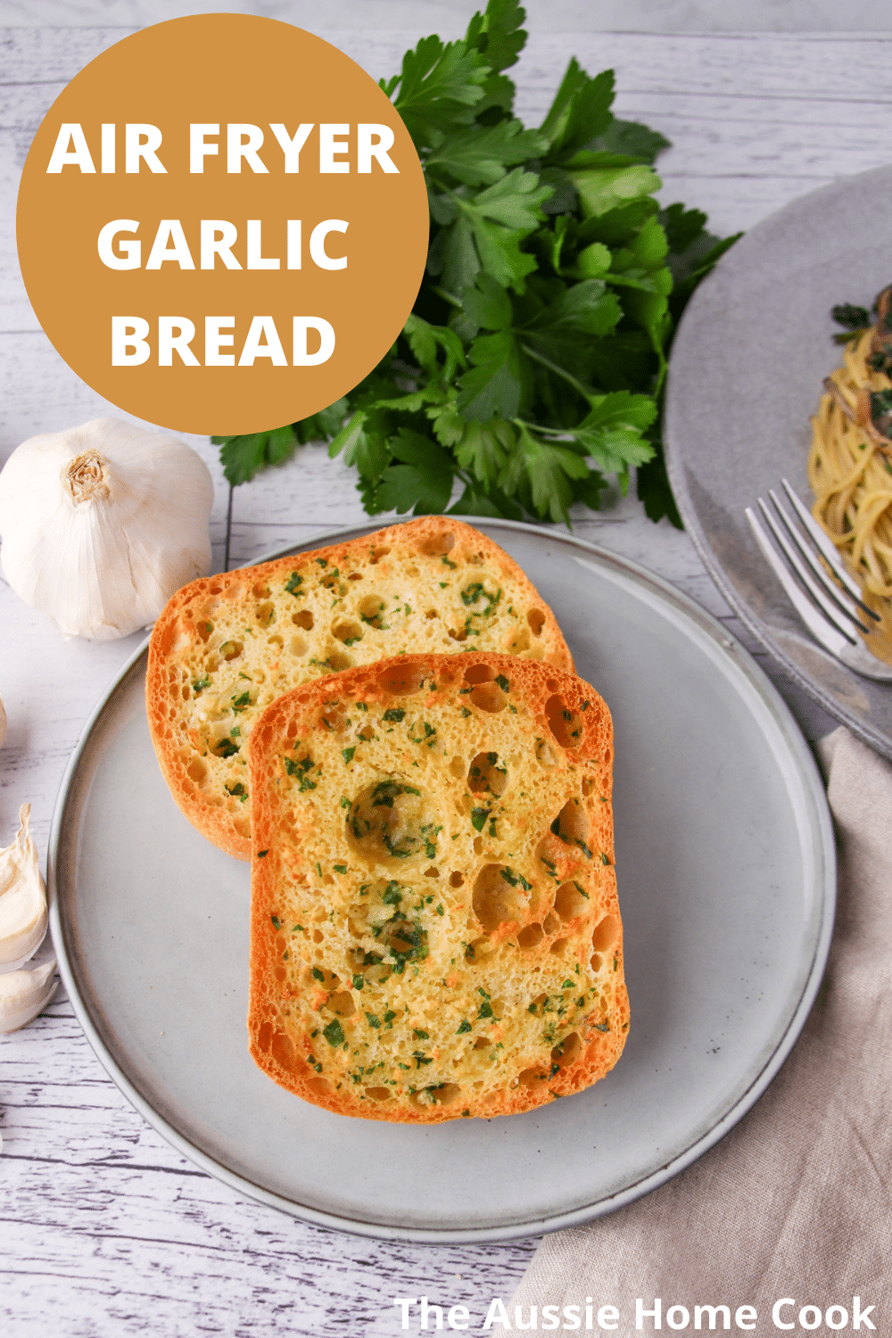 Air Fryer Garlic Bread 13 Air fryer garlic bread on a plate, with fresh garlic cloves, fresh parsley and a plate of pasta on the sides, with text overlay, Air fryer garlic bread and The Aussie Home Cook.