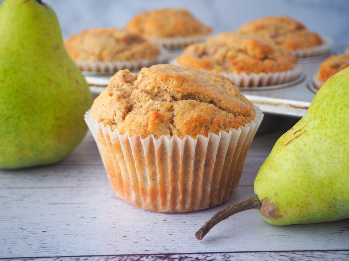 Pear muffins 1 Pear muffin with fresh pears and tray of muffins in the background.