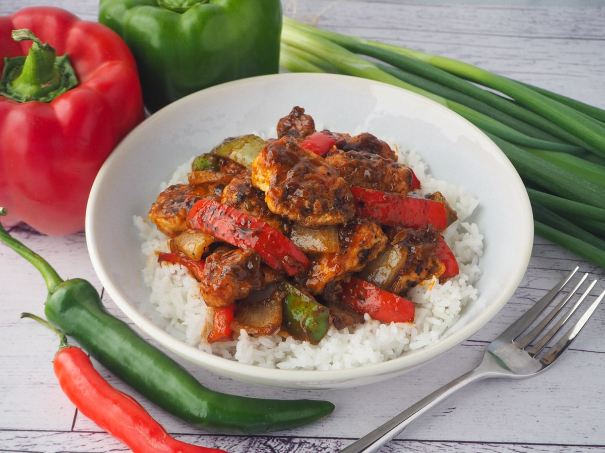 Chilli Chicken Gravy 1 Bowl of chicken on rice with fork and capsicums, spring onions and chilli on the side.
