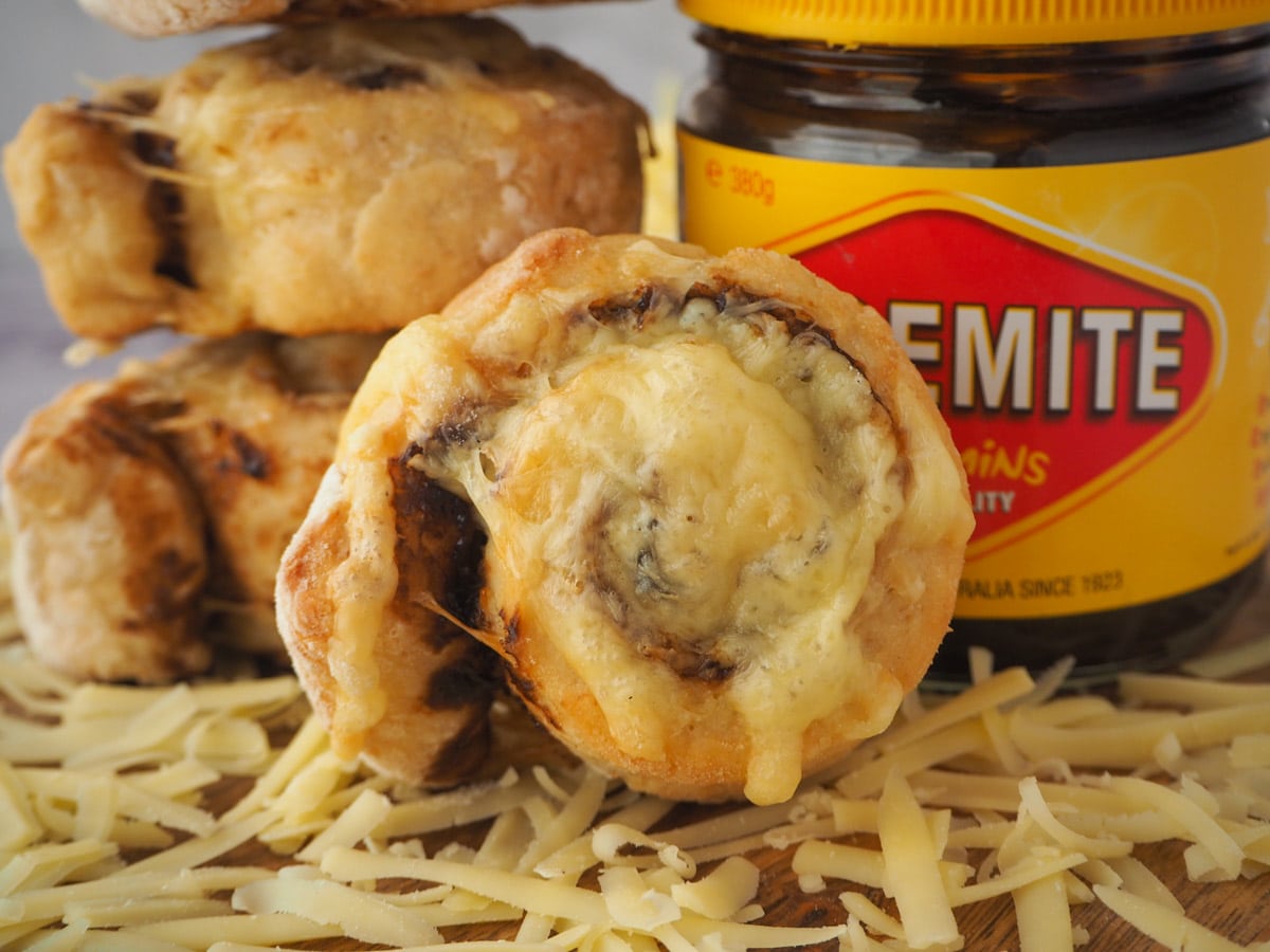 Cheesymite Scrolls 1 Scroll with stack of scrolls and jar of vegemite behind it.