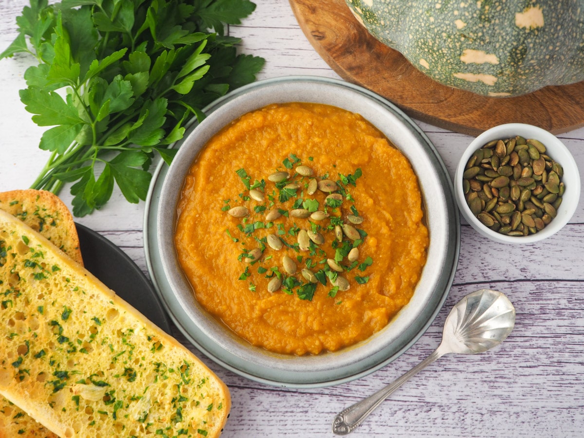 Pumpkin and Sweet Potato Soup 18 Soup with pumpkin seed and parsley garnish, with garlic bread, spoon and toasted pumpkin seeds on the side.