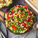 Four Bean Salad 14 Serving bowl of salad with serving spoon, knife, fork and plate on the and pie and rocket and pear salad in the background.