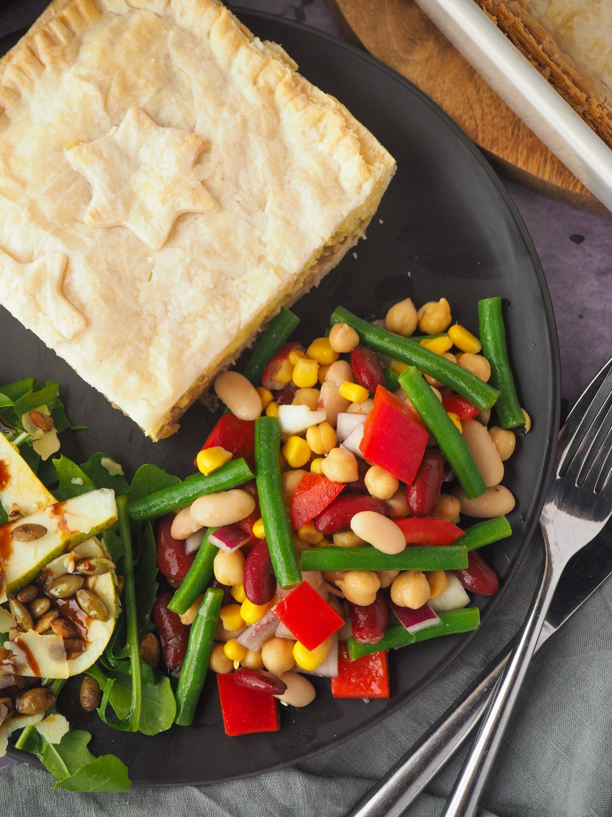 Four Bean Salad 16 Salad on a plate with a slice of pie, rocket and pear salad and knife and fork.