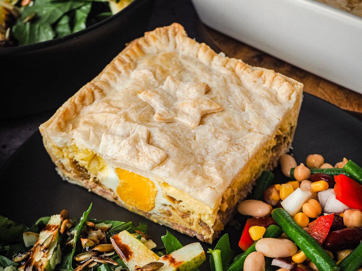 Bacon and Egg Pie 1 Pie in a plate with salads, with pie dish and salads in background.