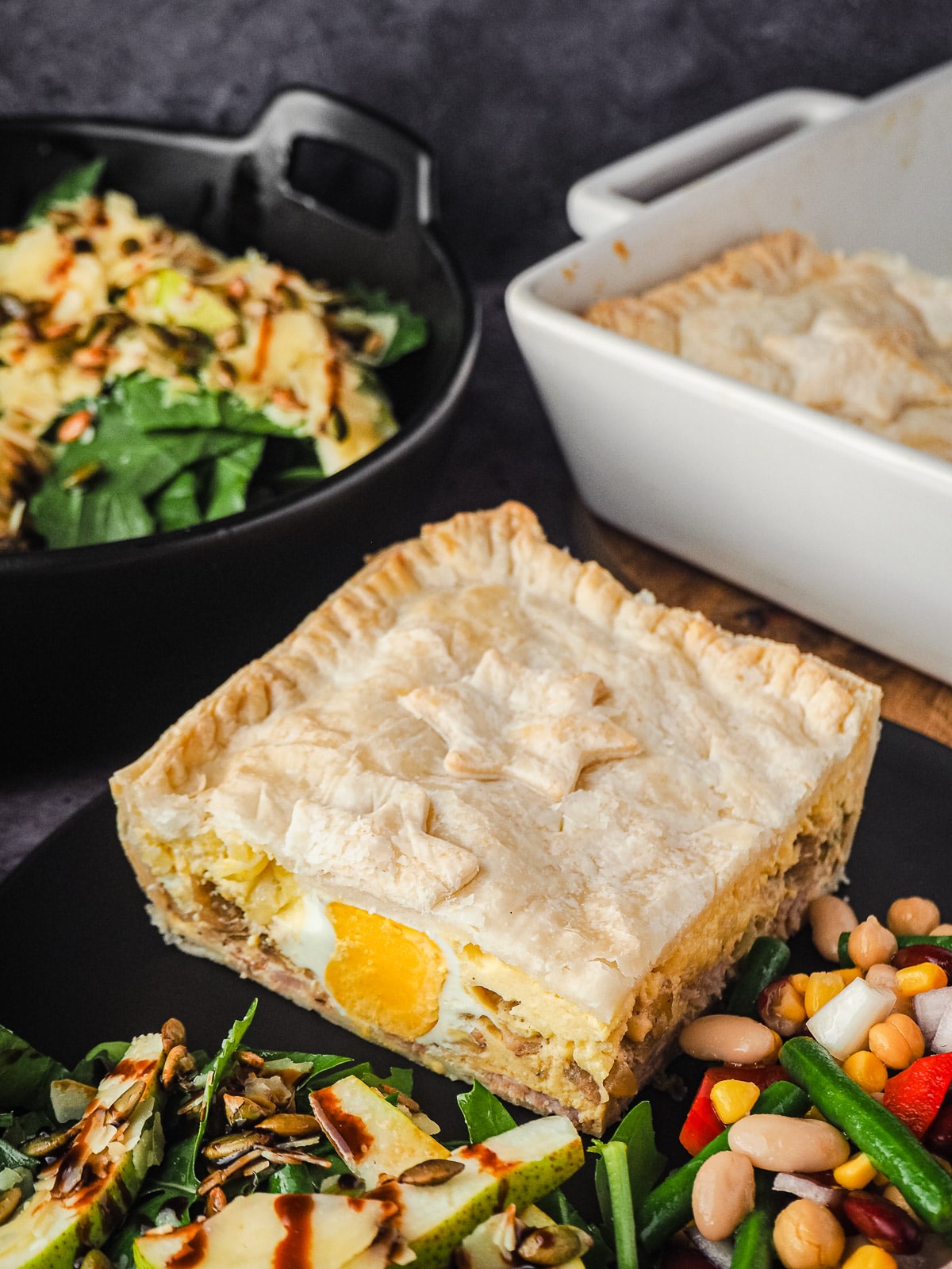 Bacon and Egg Pie 11 Pie in a plate with salads, with pie dish and salads in background.