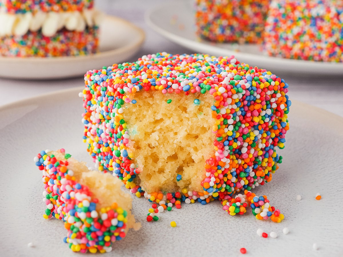 Fairy Bread Lamingtons 1 Lamington with one piece out on a plate with a fork and more lamingtons in the background.