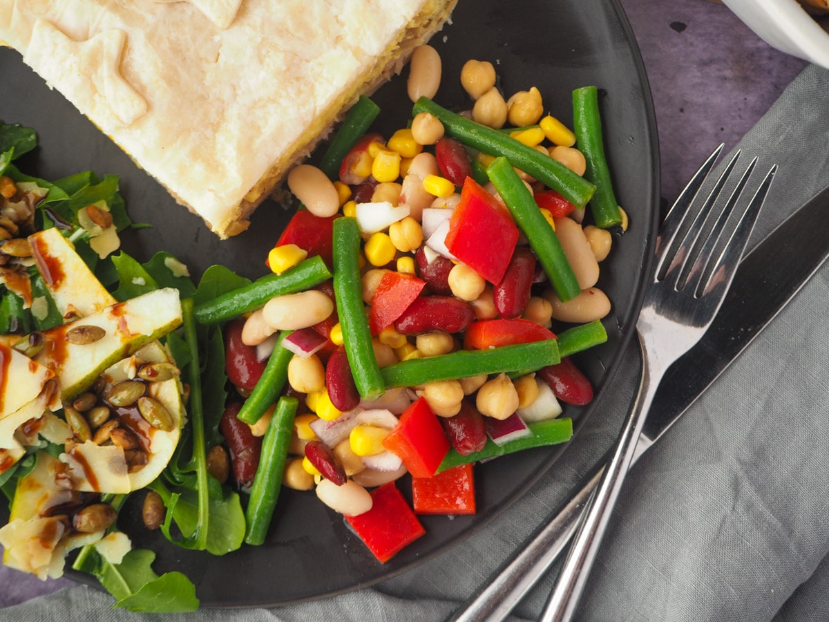 Four Bean Salad 2 Salad on a plate with a slice of pie, rocket and pear salad and knife and fork.