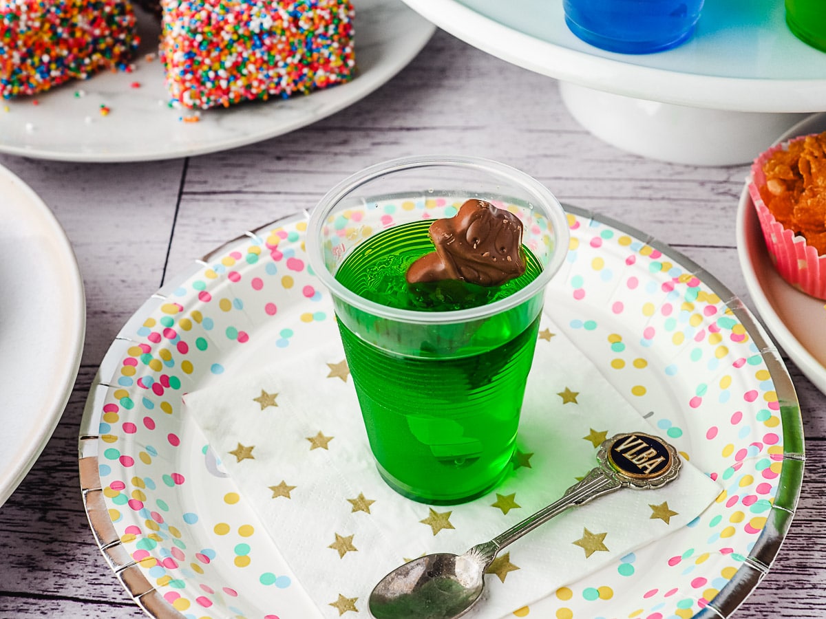 Frog In The Pond 6 Jelly cup on a party plate with a spoon and party food in the background.
