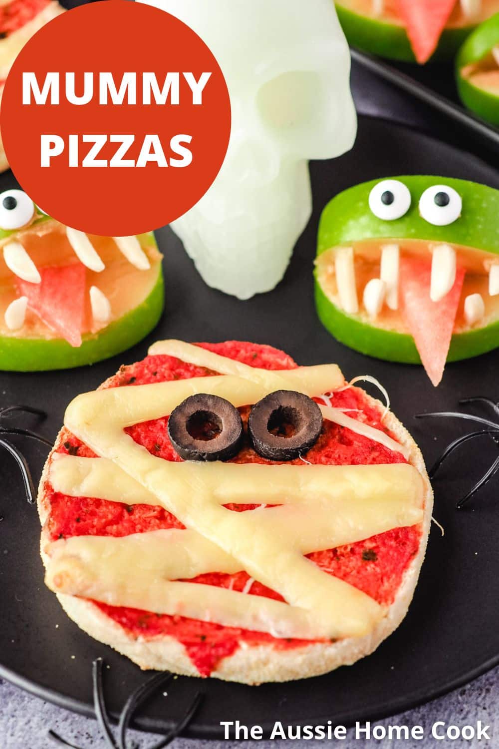 Mummy Pizzas 9 Pizza on a plate with apple monsters and skull and spider Halloween decorations, with text overlay, mummy pizzas and The Aussie Home Cook.