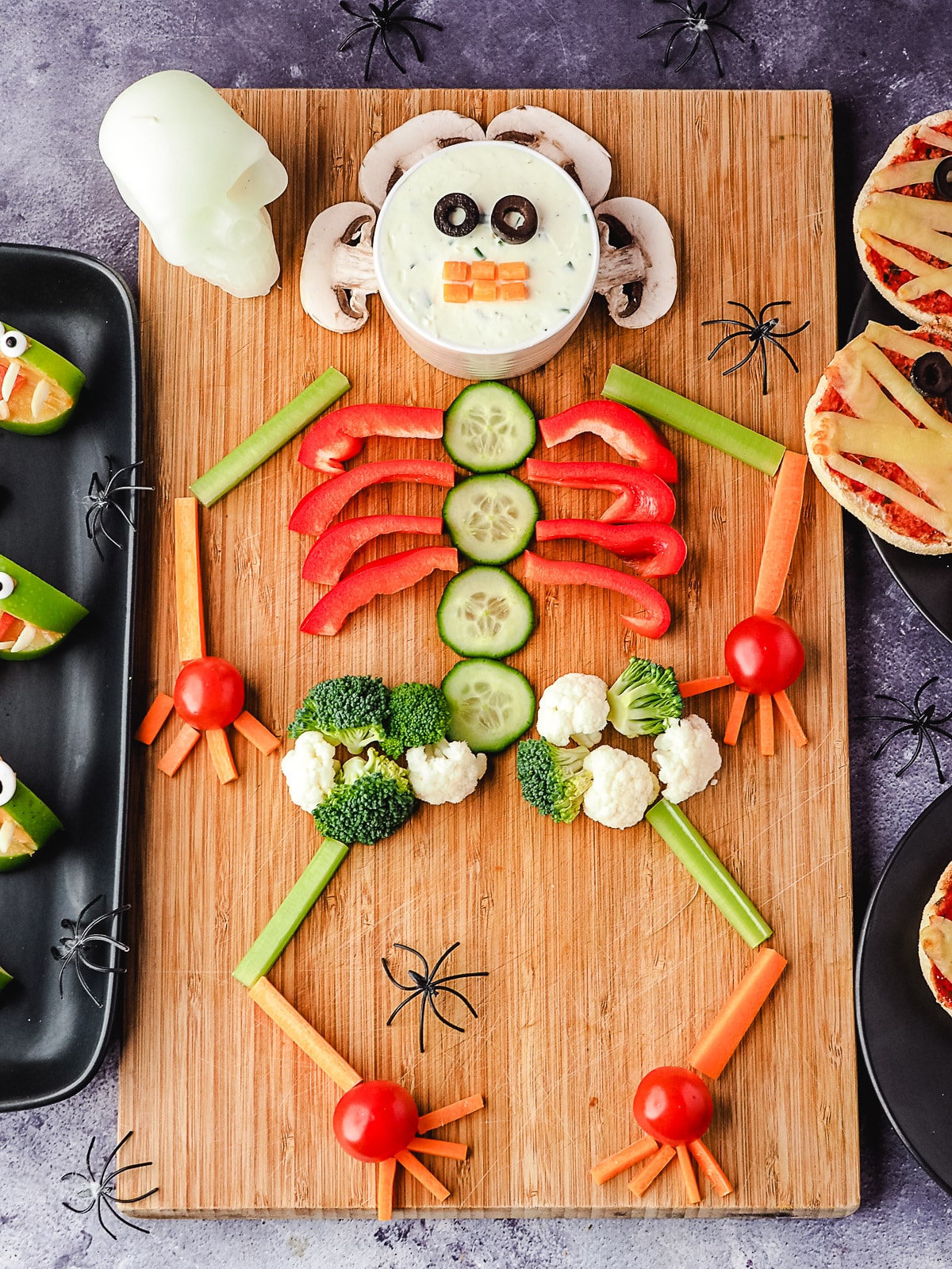 Skeleton Veggie Tray 10 Veggie tray on a board, with halloween skull and spiders, surrounded by Halloween party food, apple monsters and mummy pizzas.