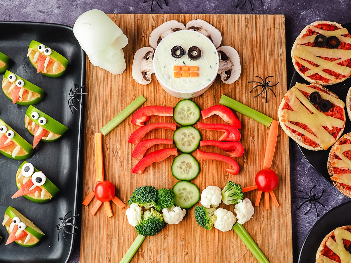 Skeleton Veggie Tray 1 Veggie tray on a board, with halloween skull and spiders, surrounded by Halloween party food, apple monsters and mummy pizzas.