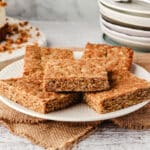 Anzac Slice 8 A pile of pieces of Anzac slice on a plate, with a pile of plates in the background.