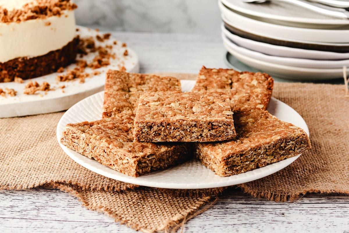 Anzac Slice 1 A pile of pieces of Anzac slice on a plate, with a pile of plates in the background.