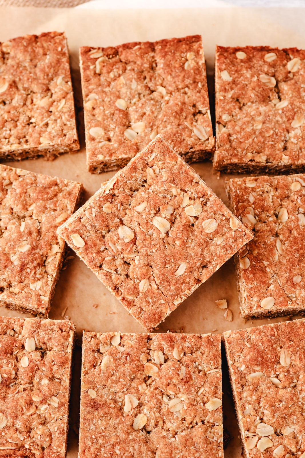 Anzac Slice 9 Top down shot of squares of Anzac slice on baking paper with the middle slice turned ninety degrees.